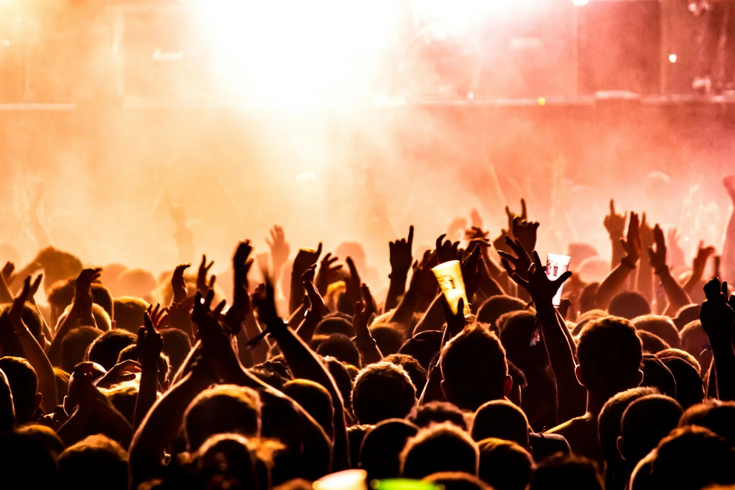 オレンジ色の照明に包まれたライブ会場で、手を上げて盛り上がる観客。